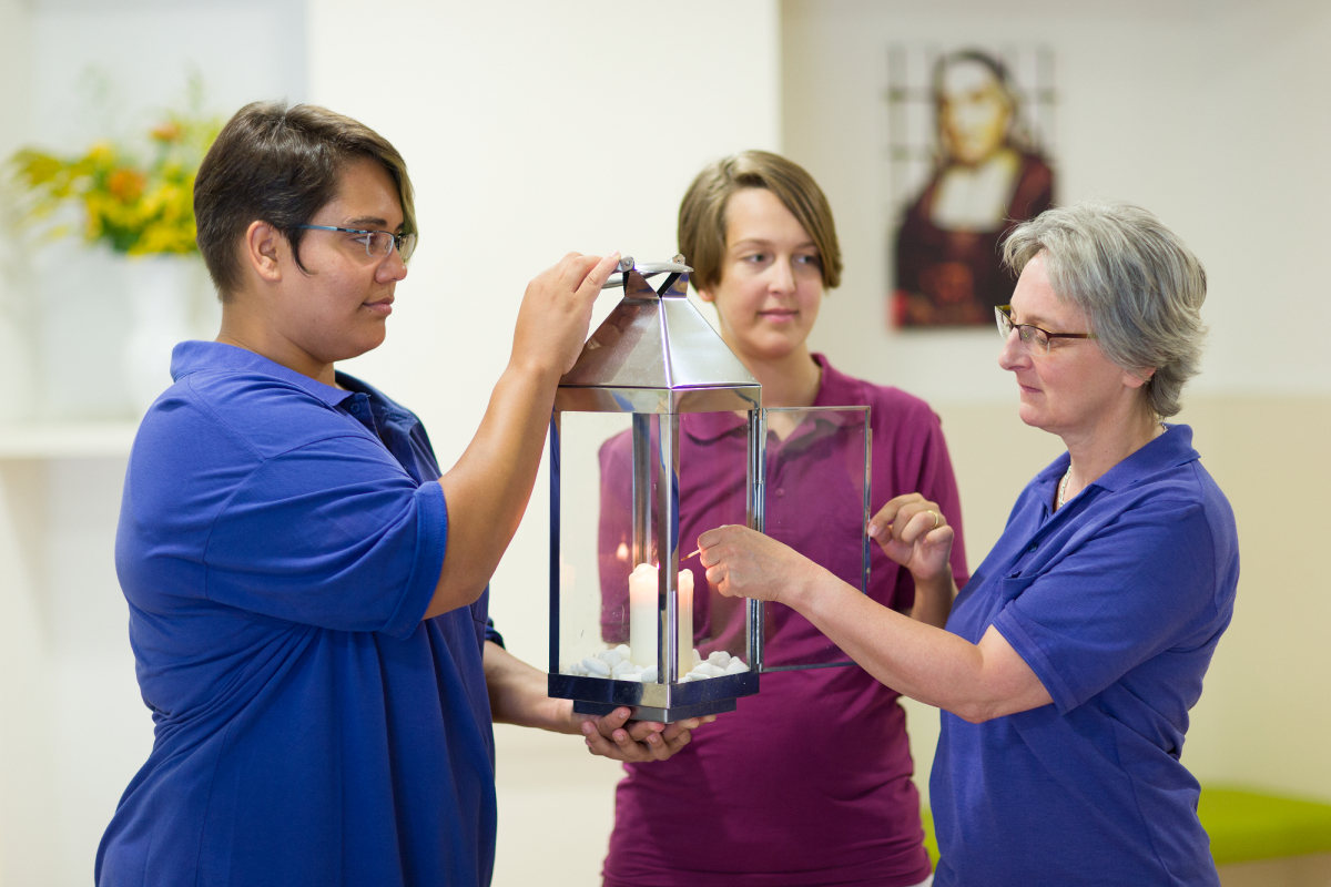 Hospiz: drei Pflegerin zünden eine Kerze an