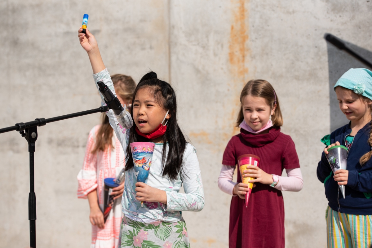 Vier Schülerinnen stehen vor einer Betonwand und halten eine kleine Schultüte in der Hand. Eine der Schülerinnen spricht in ein Mikrofon.