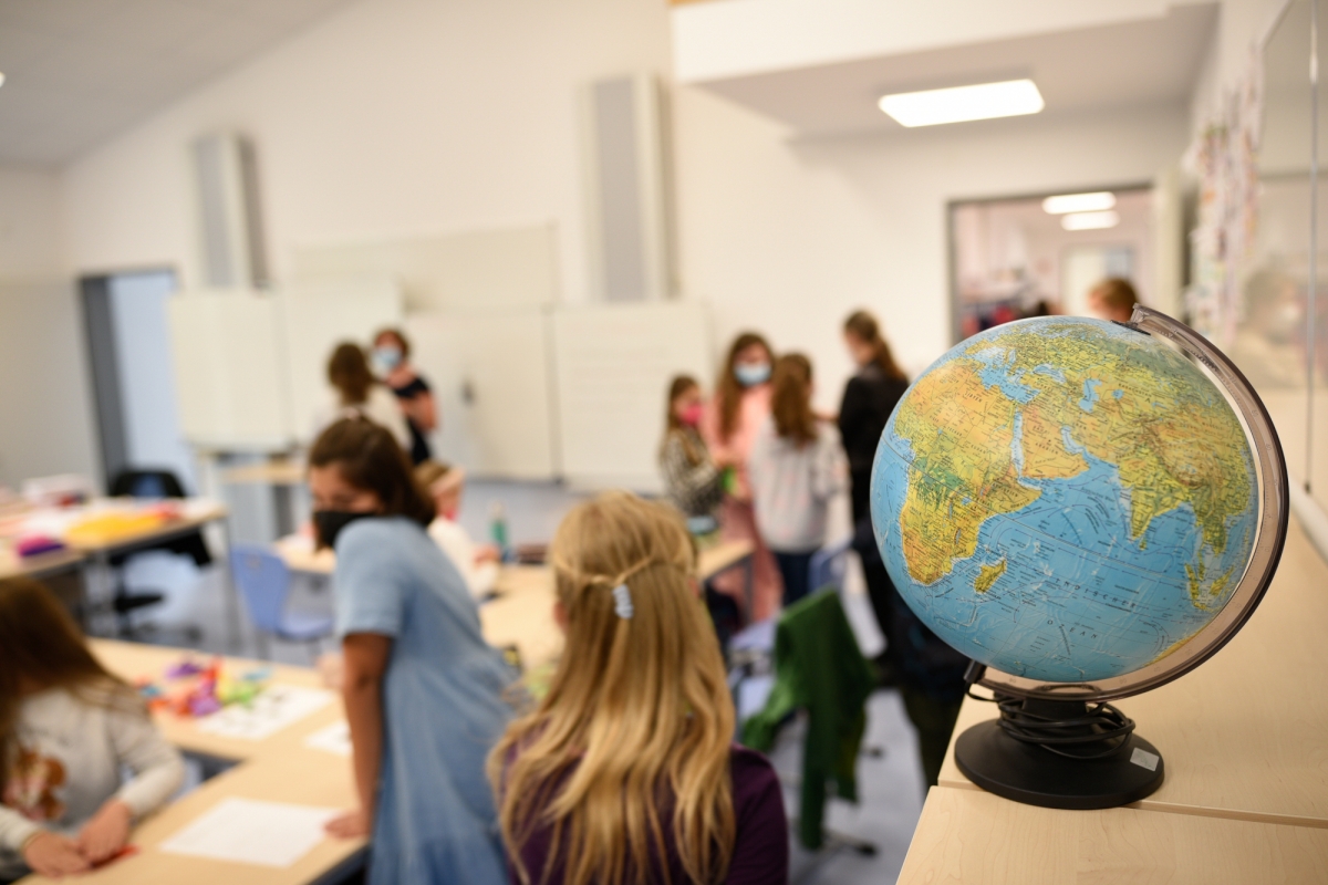 Im Vordergrund ein Globus, im Hintergrund Kinder in einem modernen Klassenzimmer.
