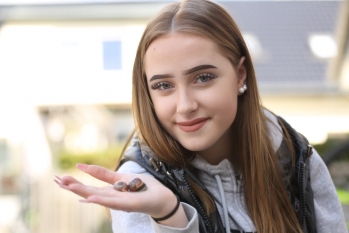 Eine Jugendliche schaut in die Kamera. Auf ihrer rechten Hand sitzen zwei Schnecken.